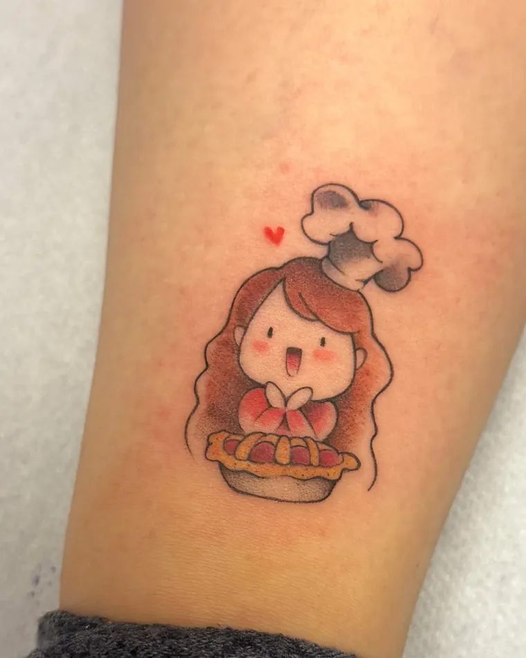 Piccolo tatuaggio a colori di una ragazza con il cappello da cuoco e una crostata
